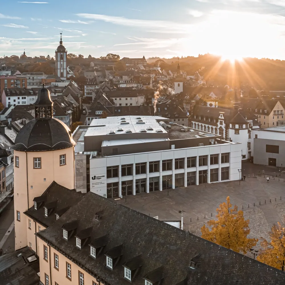 Aerial view across Siegen&rsquo;s historic city centre and the University&rsquo;s Lower Castle campus at sunset.